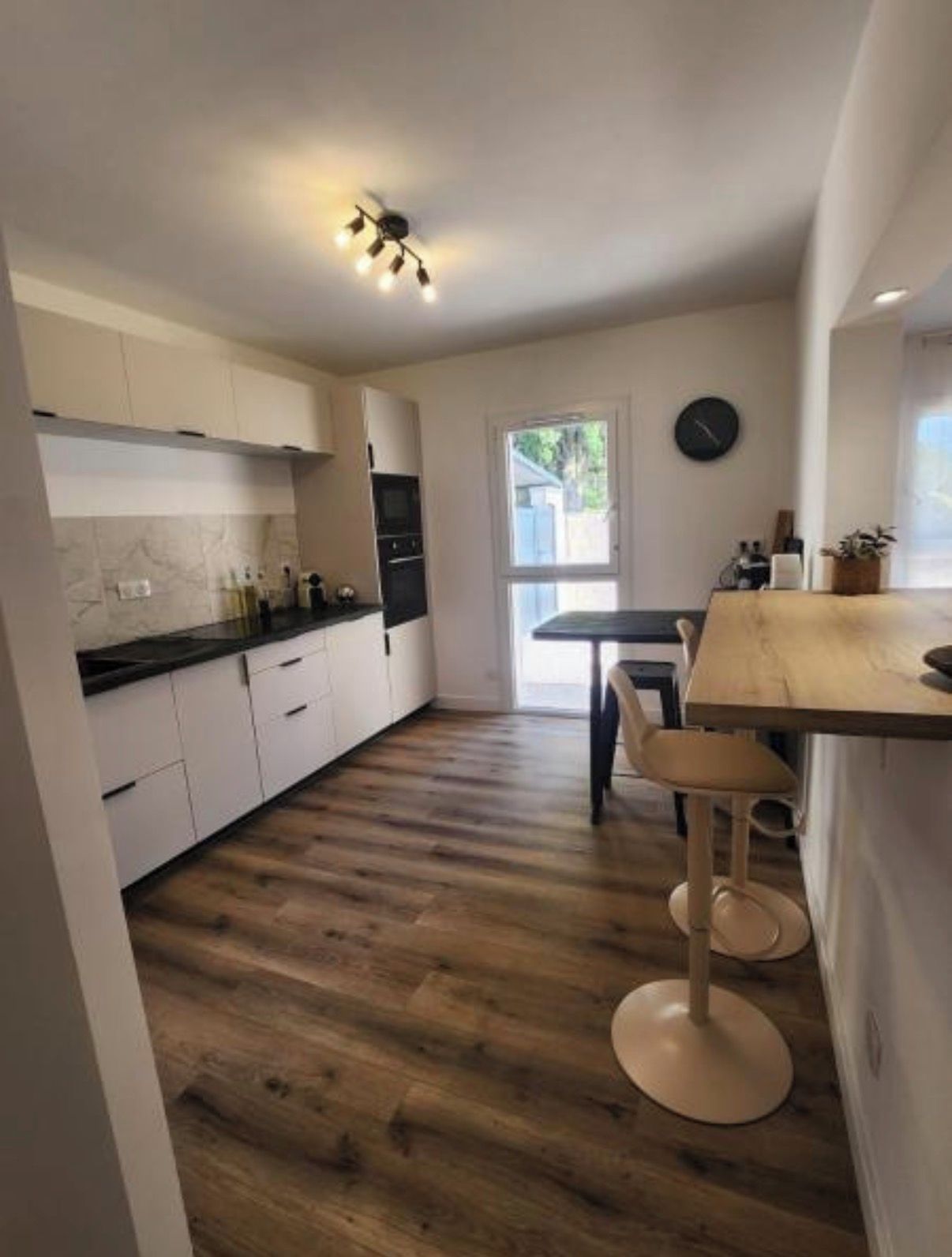 A modern kitchen with white cabinets, a wooden countertop, and a dining area with a wooden table and bar stools.
