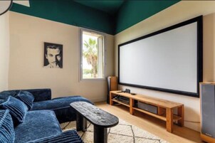Una habitación con una pantalla grande, un sofá, un banco de madera y una mesita.