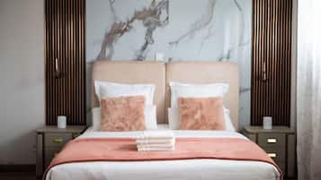 Een net opgemaakt bed met een roze en witte kleurenschema, met aan weerszijden nachtkastjes en lampen, tegen een muur met een marmerachtig patroon.