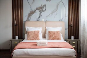 A neatly made bed with a pink and white color scheme, flanked by two bedside tables with lamps, against a wall with a marble-like pattern. - Villa Alexandre Dumas (Bussy-Saint-Georges)