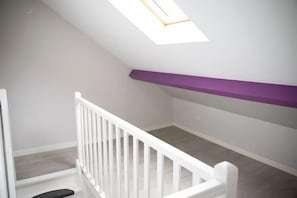 A white staircase with a white railing leading to a landing. A skylight is visible above the landing, and a purple shelf is mounted on the wall. - Villa Alexandre Dumas (Bussy-Saint-Georges)