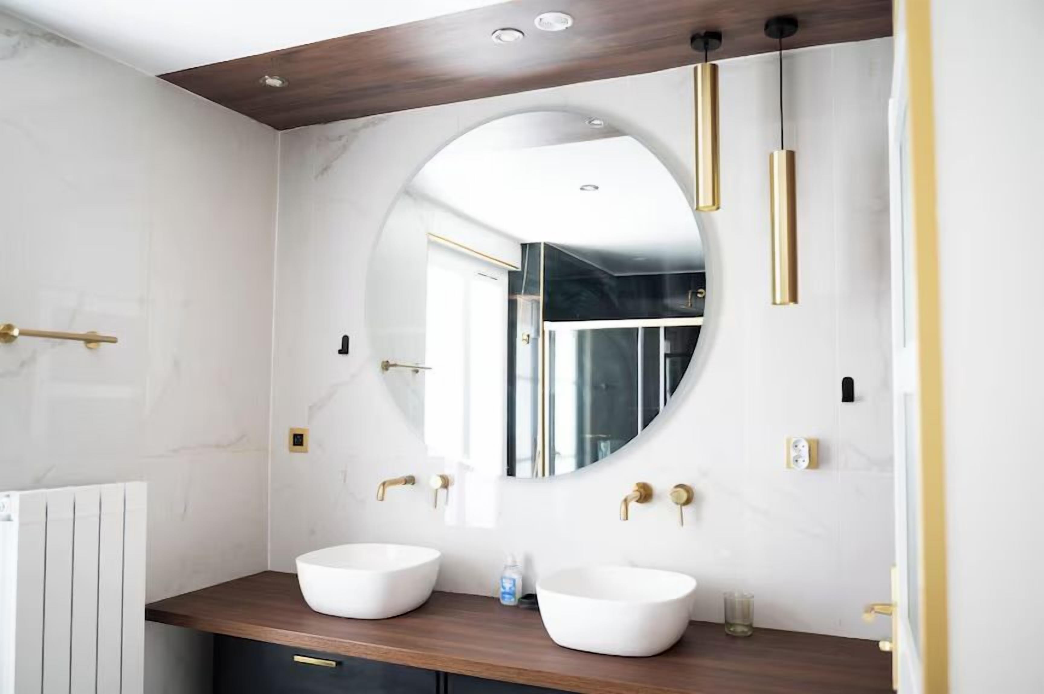A modern bathroom with two white sinks, a large mirror, and gold fixtures.