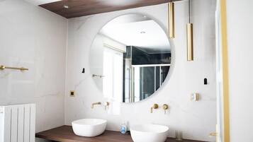 A modern bathroom with two white sinks, a large mirror, and gold fixtures.