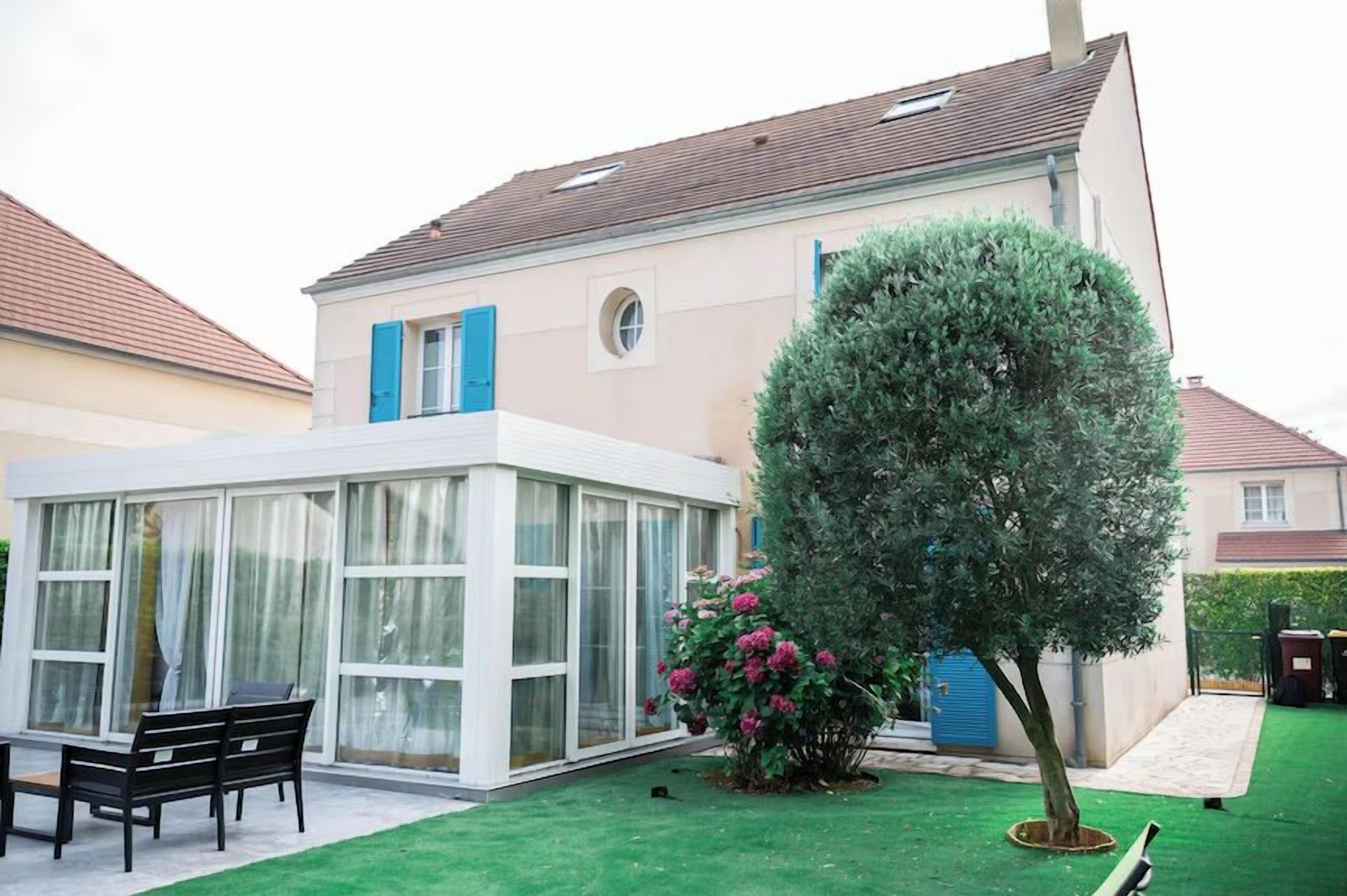 Ein modernes Haus mit Wintergarten, einem gepflegten Rasen und einem großen Baum.