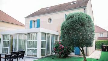 Ein modernes Haus mit Wintergarten, einem gepflegten Rasen und einem großen Baum.