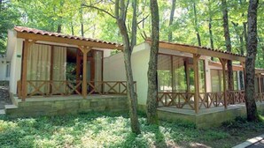 A row of wooden cabins with a covered porch, surrounded by trees. - Villas Holidays (Kiten)