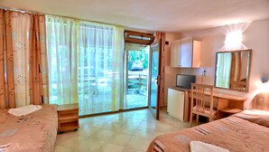 A hotel room with two beds, a desk, a chair, a television, and a sliding glass door leading to an outdoor area. - Villas Holidays (Kiten)