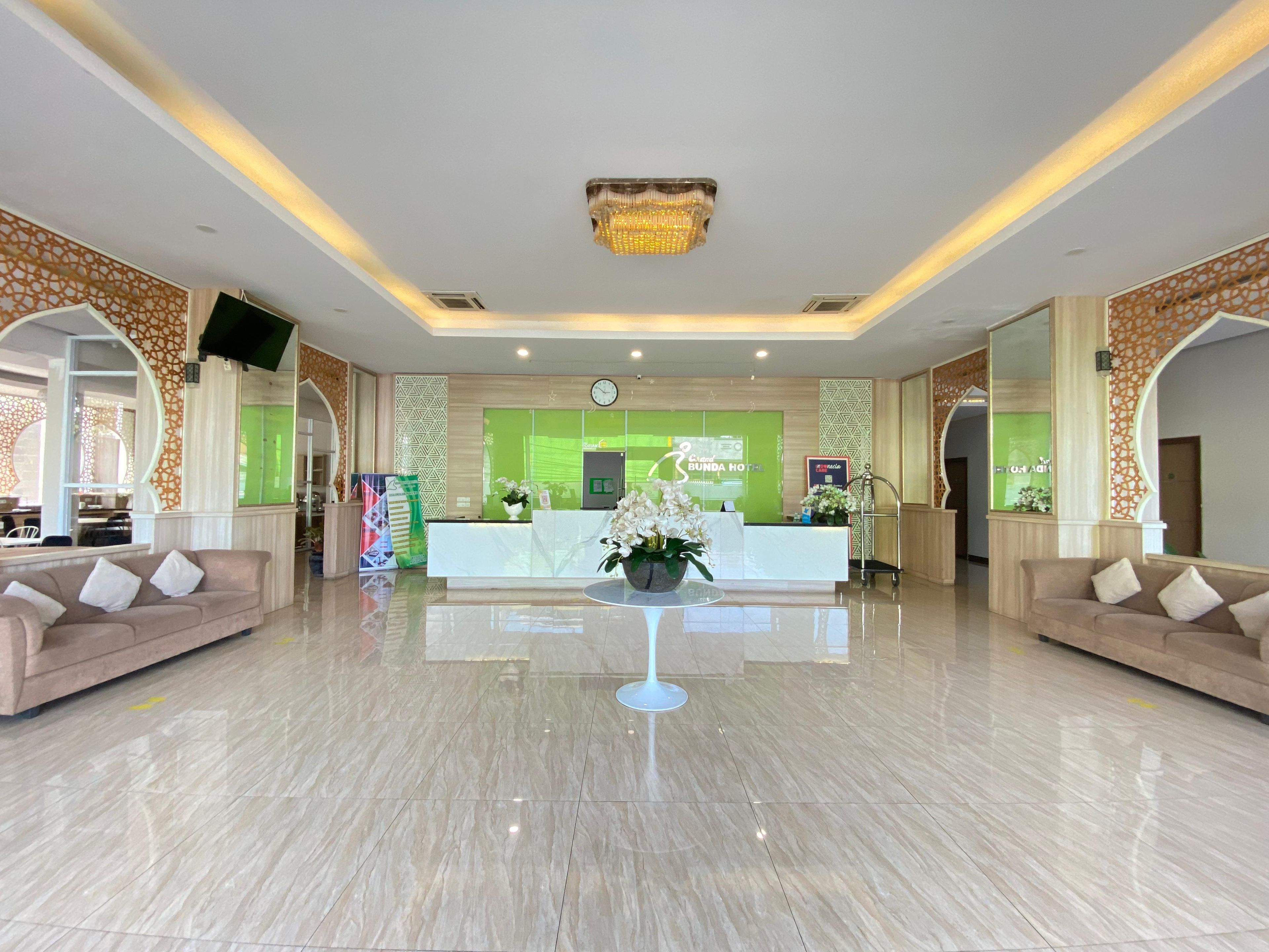 A hotel lobby with a reception desk, two sofas, a chandelier, and a clock on the wall.