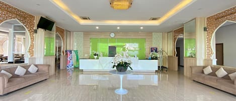A hotel lobby with a reception desk, two sofas, a chandelier, and a clock on the wall.