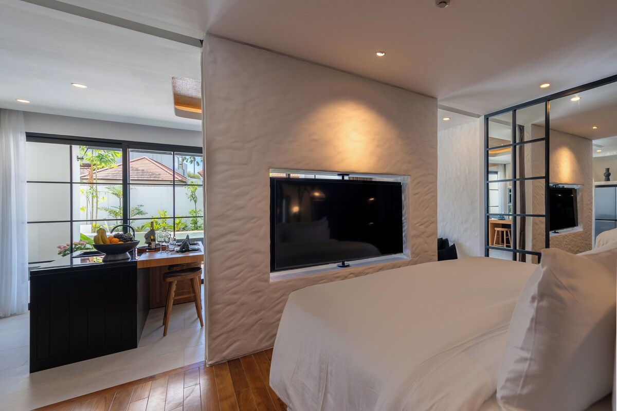 Une chambre moderne avec un grand lit, un téléviseur fixé au mur et un bureau donnant sur l’extérieur.