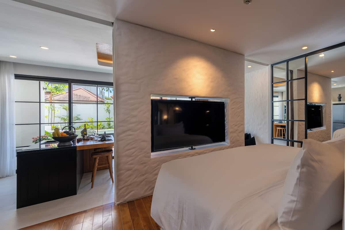 A modern bedroom with a large bed, a TV mounted on the wall, and a desk with a view to the outside.