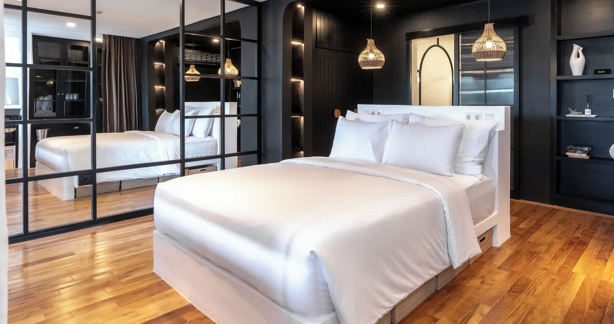 Ein modernes Schlafzimmer mit einem großen Bett, Schranktüren mit Spiegeln und Pendelleuchten.