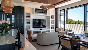 A modern living room with a flat-screen TV, comfortable seating, and a dining area with a table and chairs.