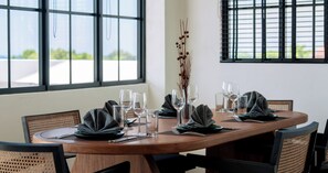 A dining table set with plates, glasses, and cutlery, surrounded by wicker chairs. - Kiara Ocean Place (Tibubeneng)
