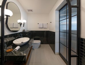 A modern bathroom with a round mirror, a sink, a toilet, and a shower area. - Kiara Ocean Place (Tibubeneng)