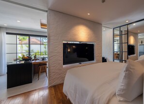 A modern bedroom with a large bed, a TV mounted on the wall, and a desk with a view to the outside. - Kiara Ocean Place (Tibubeneng)
