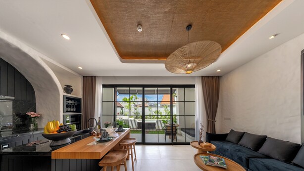 A modern kitchen with a central island, a dining area with a wooden table and chairs, and a living area with a dark blue sofa and a wooden coffee table.