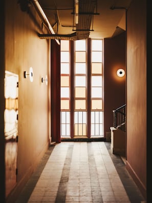 Un couloir avec une grande fenêtre, un escalier et une porte avec un rideau.