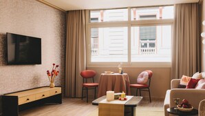 Una sala de estar moderna con un televisor de pantalla plana, una mesa de centro de madera, dos sillones, un sofá y una pequeña mesa con velas y libros.