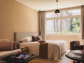 Habitación de hotel con cama, sofá, una mesita y ventana con vistas a edificios.