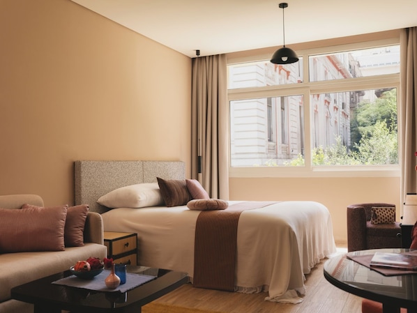 Une chambre d’hôtel avec un lit, un canapé, une petite table et une fenêtre donnant sur des immeubles.
