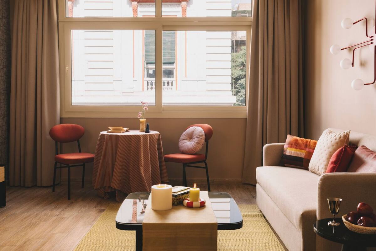Una sala de estar acogedora con un sofá, dos sillones, una mesa de centro y una ventana con cortinas.