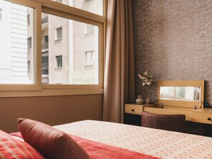 Habitación de hotel con cama, escritorio y ventana con cortinas.
