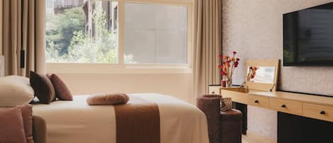 Un dormitorio con una cama grande, televisión, escritorio y ventana con vistas a la vegetación.