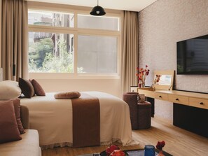 Un dormitorio con una cama grande, televisión, escritorio y ventana con vistas a la vegetación.