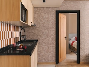 A modern kitchen with a black countertop, wooden cabinets, and a patterned wallpaper. A door leads to a bedroom with a bed and a red pillow. - Saint J Hotel By Brassbell (Cairo)