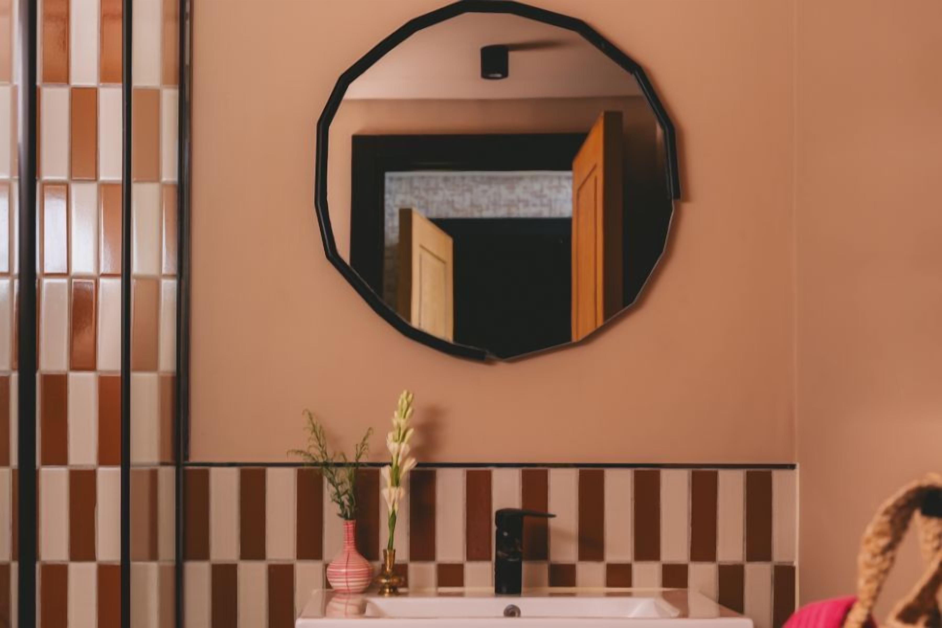 Un baño con un espejo redondo, un lavamanos blanco y un salpicadero de azulejos.