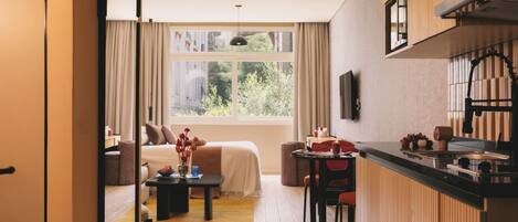 A modern hotel room with a bed, a dining area, and a kitchen.
