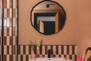 Une salle de bain avec un miroir rond, un lavabo et un mur recouvert de carreaux.