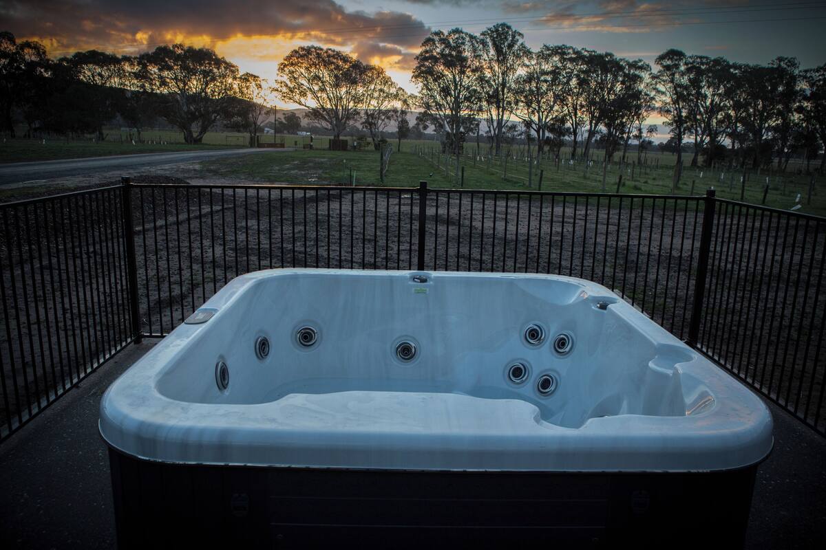 Un jacuzzi con barandilla de metal, rodeado por un patio cercado con árboles y una carretera al fondo.