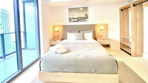 A modern hotel room with a large bed, two bedside tables with lamps, a view of the city through large windows, and a wooden wardrobe. - Nice 2Bdrm Unit - Downtown Miami (Miami)