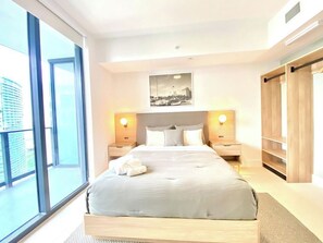 A modern hotel room with a large bed, two bedside tables with lamps, a view of the city through large windows, and a wooden wardrobe. - Nice 2Bdrm Unit - Downtown Miami (Miami)
