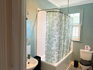 Ein Badezimmer mit Duschvorhang, Toilette, Waschbecken und Fenster.