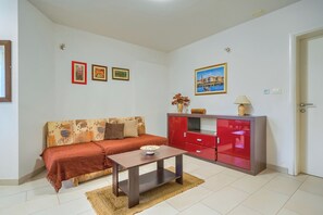 A living room with a sofa, a coffee table, a red cabinet, and wall art. - A comfortable apt w balcony, 4 min walk to beach (Split)