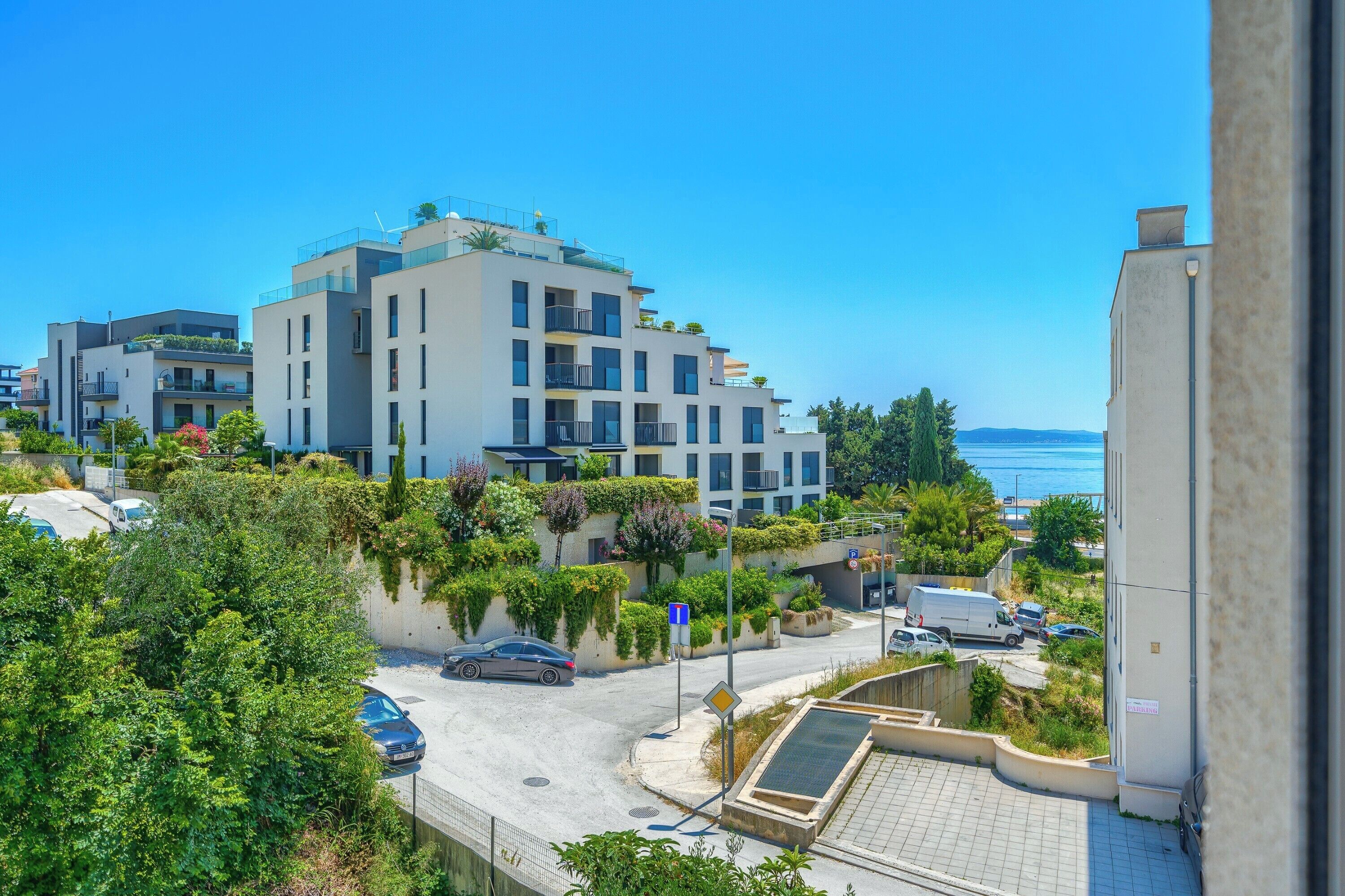 A modern apartment building with balconies, a parking area, and a view of the sea.