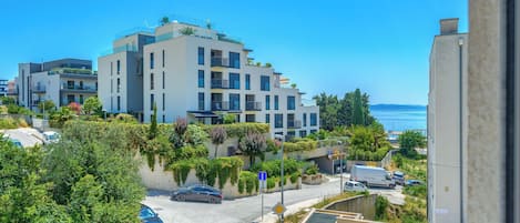 A modern apartment building with balconies, a parking area, and a view of the sea.