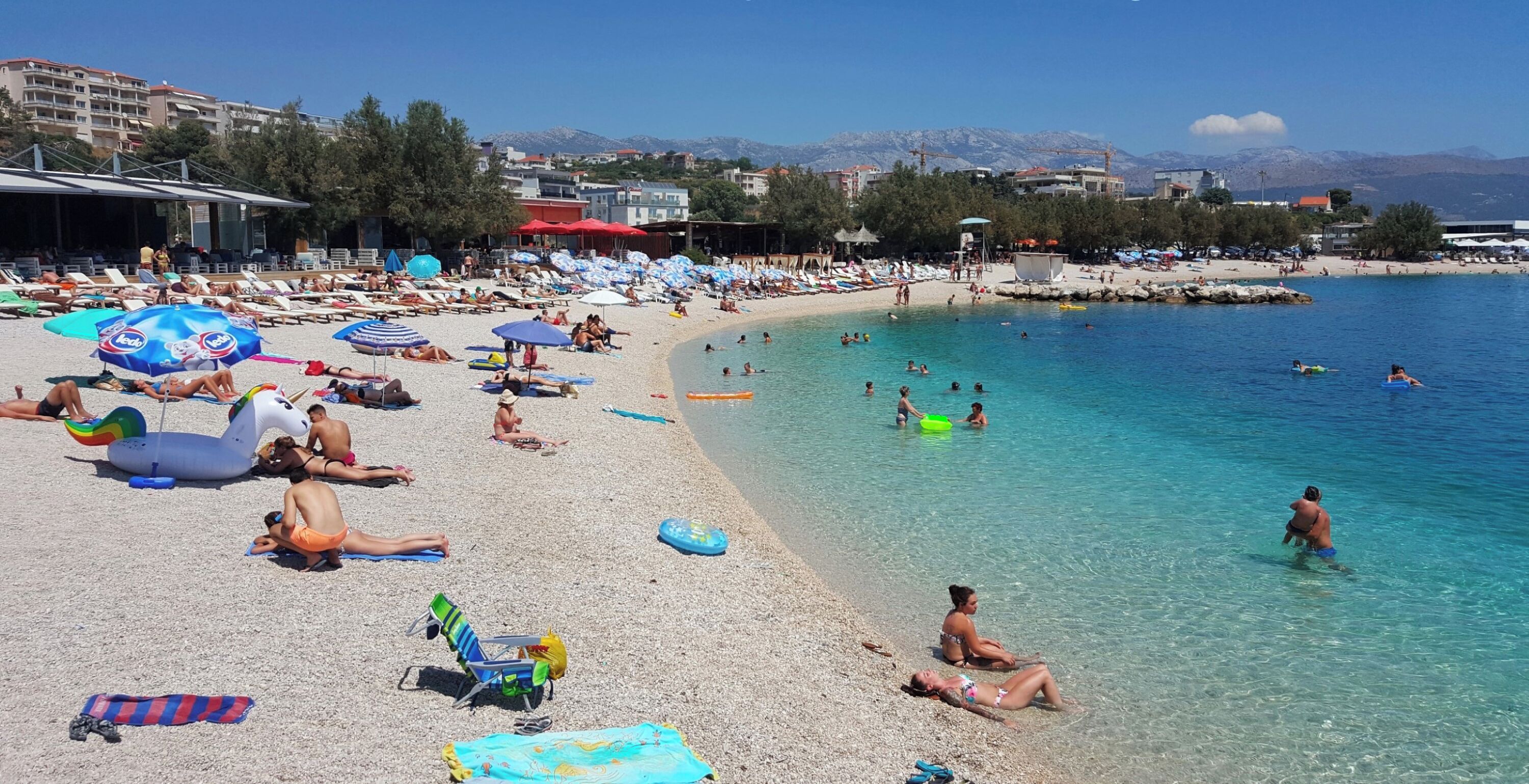 Une plage avec des transats, des parasols et des gens qui se baignent.