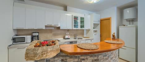 Cozinha moderna com armários brancos, micro-ondas embutido, cafeteira e ilha de pedra com jogos americanos trançados.