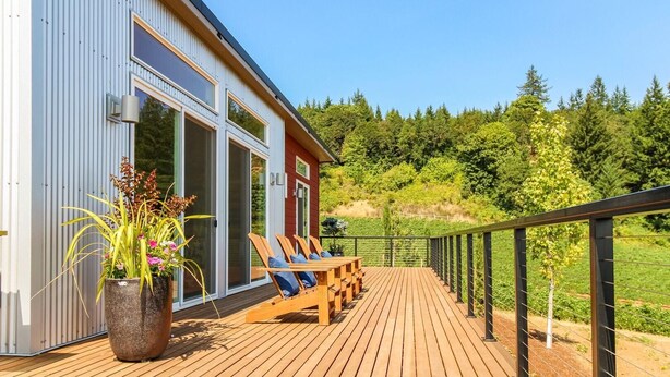 A wooden deck with outdoor seating, a large window, and a view of a forested hillside. - The View House at Bryn Mawr Vineyards (Salem)