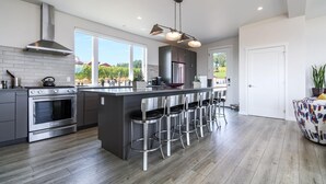 A modern kitchen with a large island, stainless steel appliances, and a bar area with stools. - The View House at Bryn Mawr Vineyards (Salem)