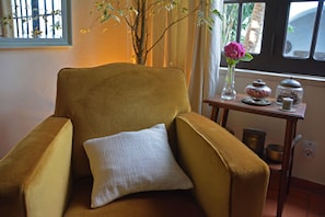 A mustard-colored armchair with a white pillow, a vase with a pink flower, and a small wooden table with jars and a bowl. - Charming Obidos House with 3 Bedrooms (Obidos)