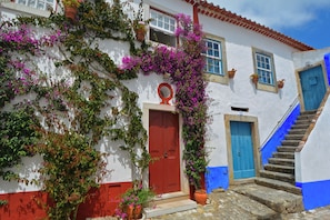 A white building with a red door, blue windows, and a blue staircase. - Charming Obidos House with 3 Bedrooms (Obidos)