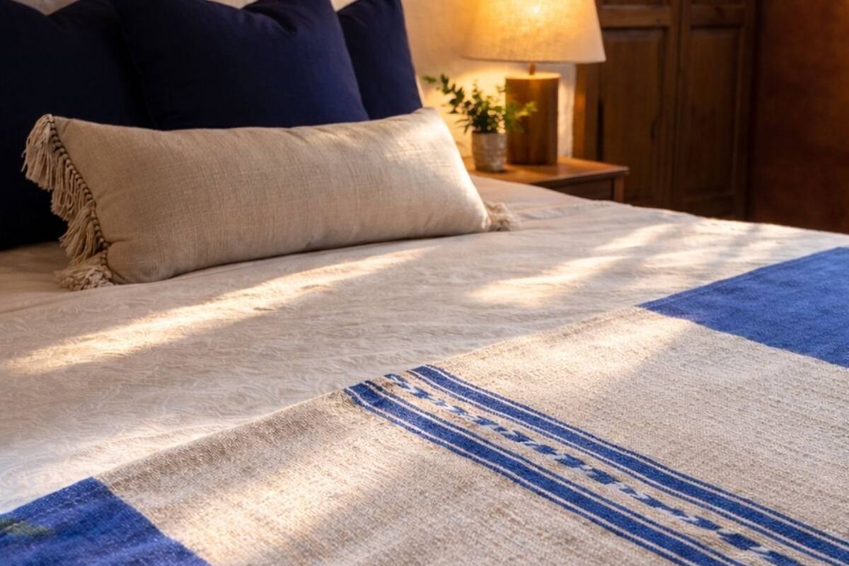 Un llit ben fet amb llençols estampats, almoinos i una làmpada de nit.