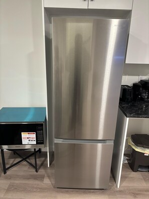 Ein Edelstahl-Kühlschrank mit digitaler Anzeige, eingebaut in eine Küche mit türkisfarbener Arbeitsplatte und einem schwarzen Unterschrank.