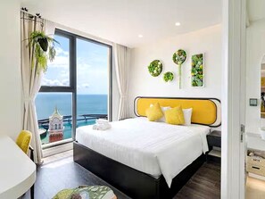 Camera d'albergo con un grande letto, vista sul mare e un balcone con vista su un edificio.