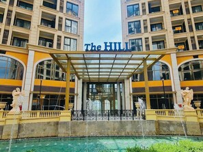 A hotel entrance with a covered entrance, a fountain, and statues.